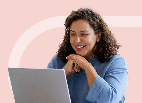 Woman in blue looking at silver laptop smiling.