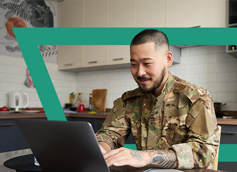 Man wearing Army fatigues using laptop in kitchen.