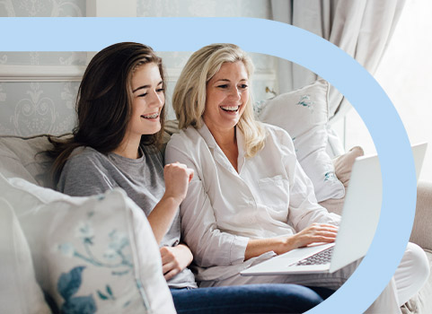 Mom and daughter sitting on couch using white laptop.