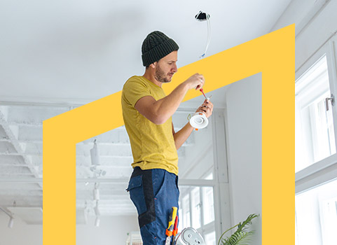 Man in yellow shirt fixing light fixture.