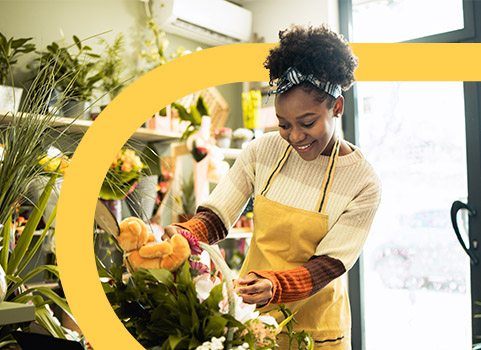 Woman in yellow apron arranging flowers.