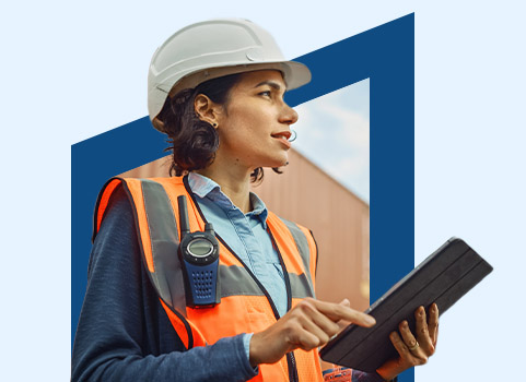 Woman in orange safety vest and white hard hat using tablet.