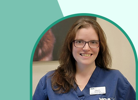 A woman with fair skin and light brown hair wearing scrubs and glasses smiles at the camera