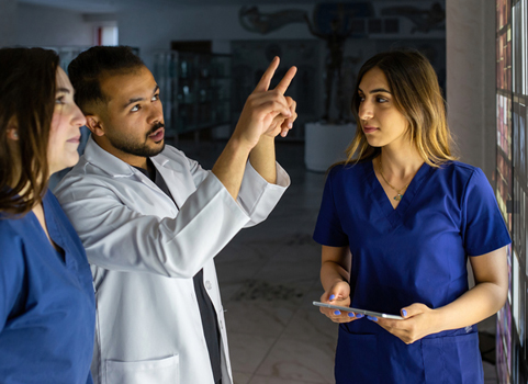 One person in a lab coat points at something, while two other people in scrubs look on