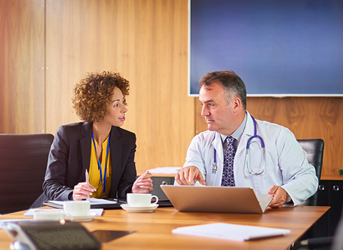 Two people sit in a boardroom, discussing something on a computer screen